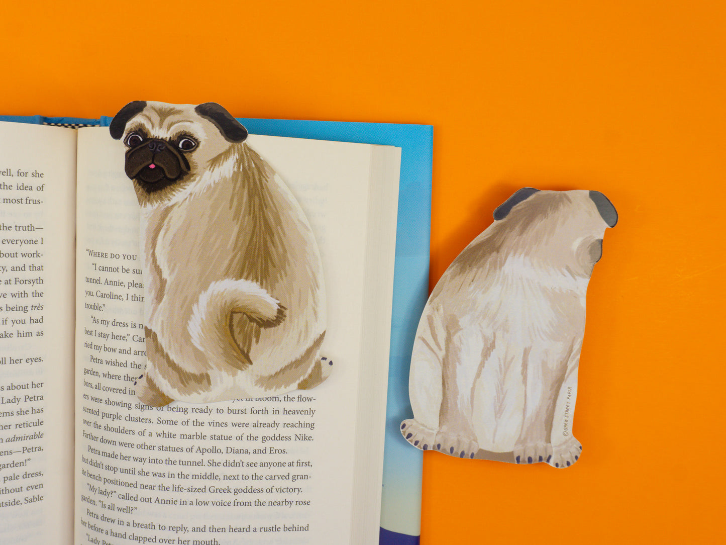 Cream pug bookmark positioned on top of a book on orange background