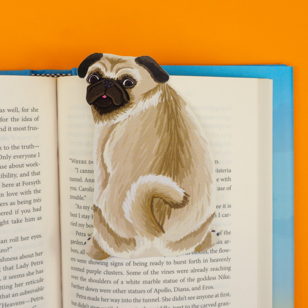 Cream pug bookmark with black face and wrinkles marking page in book on orange background