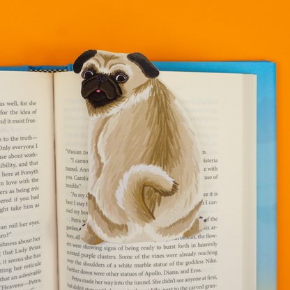 Cream pug bookmark with black face and wrinkles marking page in book on orange background