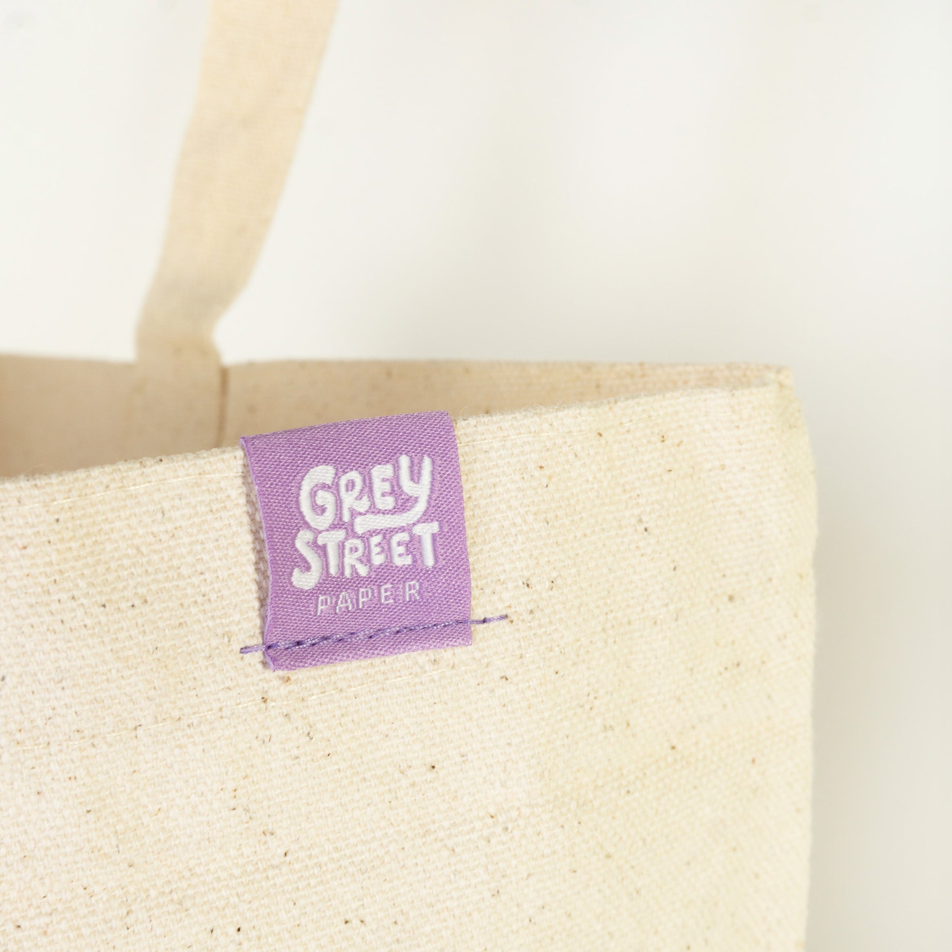 Close-up of Grey Street Paper purple woven label tag sewn on natural cotton tote bag