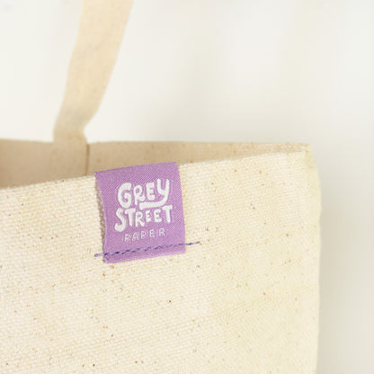 Close-up of Grey Street Paper purple woven label tag sewn on natural cotton tote bag