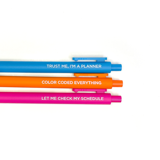 Three colorful pens stacked saying 'TRUST ME, I'M A PLANNER' in blue, 'COLOR CODED EVERYTHING' in orange, and 'LET ME CHECK MY SCHEDULE' in hot pink on white background