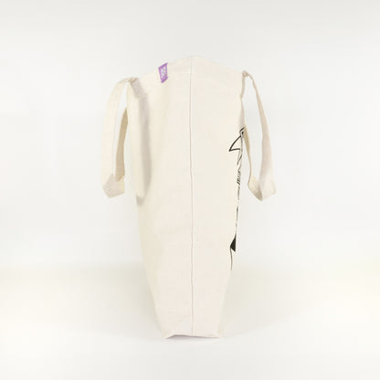 Side view of I'd Rather Be Reading cotton tote bag showing partial book stack design and Grey Street Paper purple label tag on natural canvas