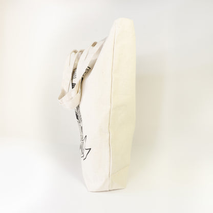 Side profile of I'd Rather Be Reading cotton tote bag showing edge of book illustration and ribbon banner on natural canvas