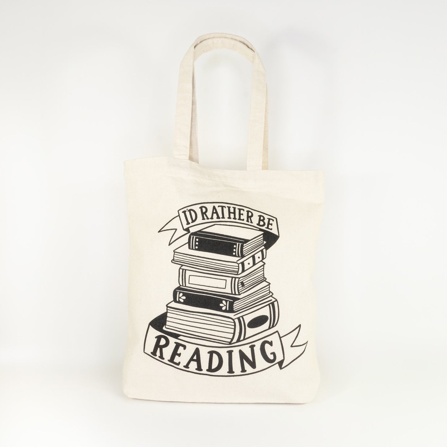 Front view of I'd Rather Be Reading cotton tote bag laying flat showing complete design with stack of books between ribbon banners on natural canvas