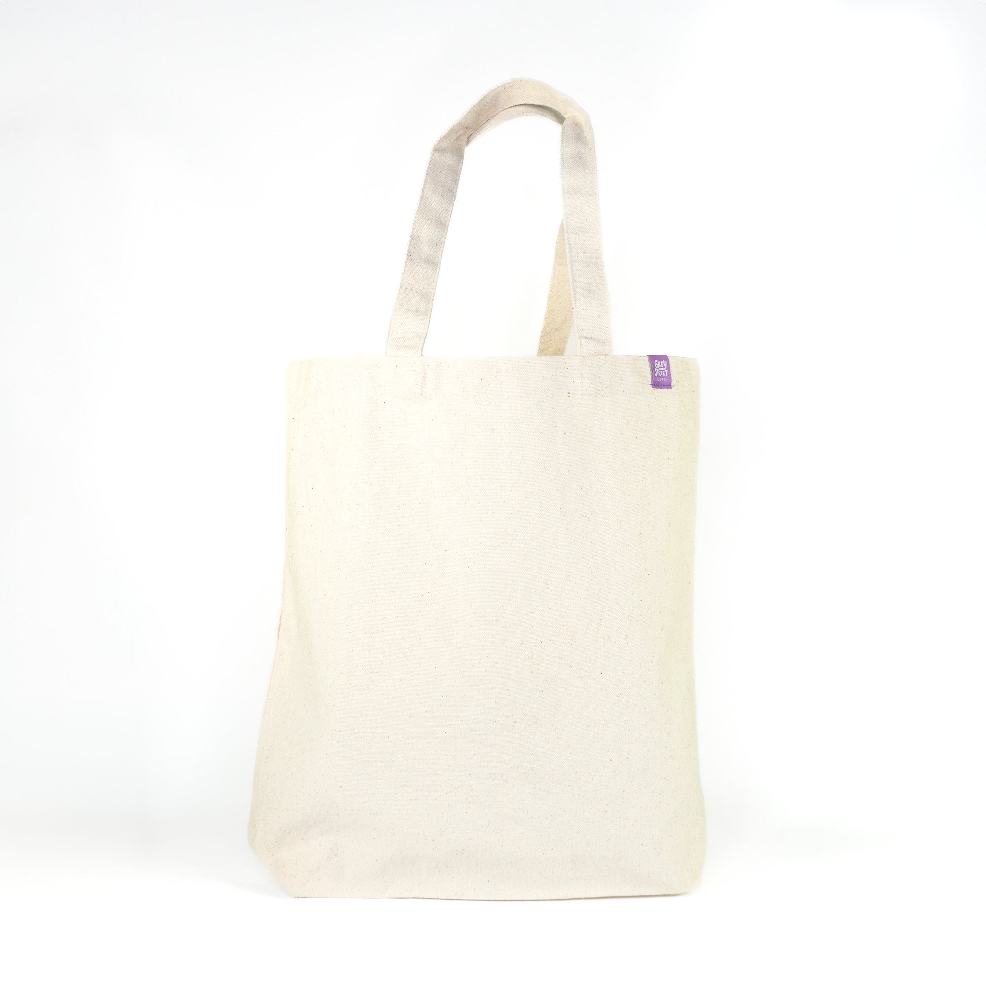 Back view of natural cream cotton tote bag with Grey Street Paper purple label tag on white background