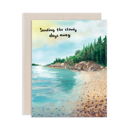 Greeting card with a serene beach scene with pine trees in the background and text 'Sending the cloudy days away' on a white background.